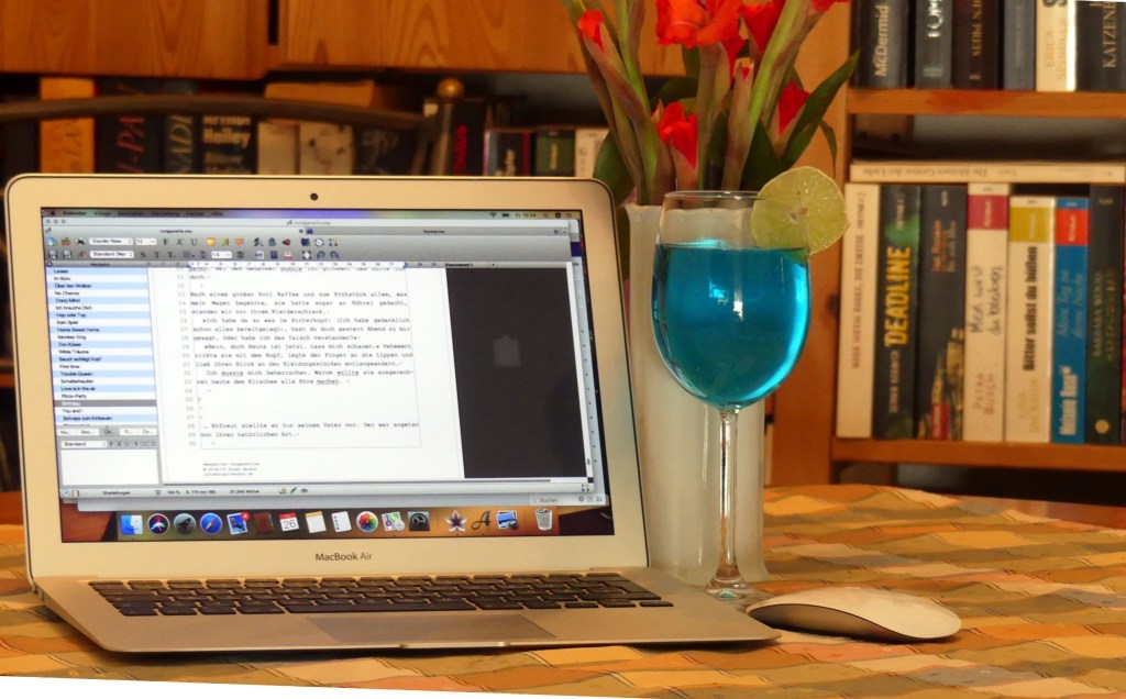 A computer screen with a manuscript on it, next to a blue glass of alcohol, 