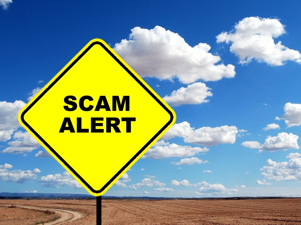A yellow warning sign that reads "Scam Alert" set across a blue sky
