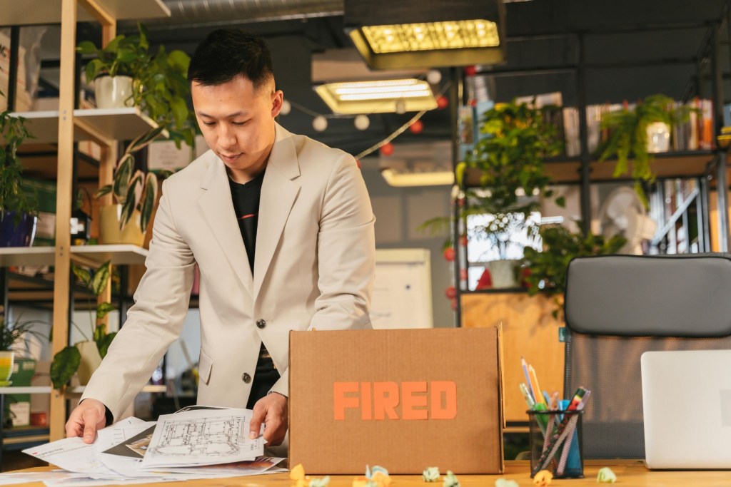 A freelance worker packing up his desk  with a box that says "fired" on it.