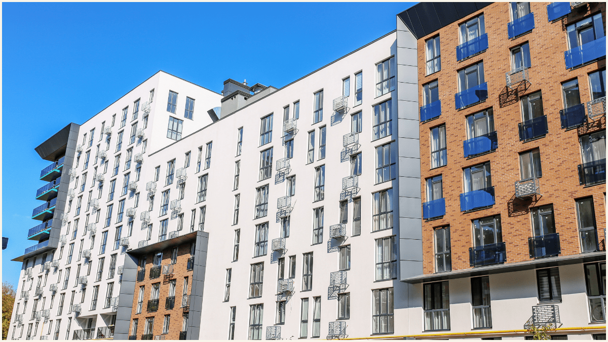 Modern apartment buildings with white and brick facades, balconies with railings, and many windows under a clear blue sky.