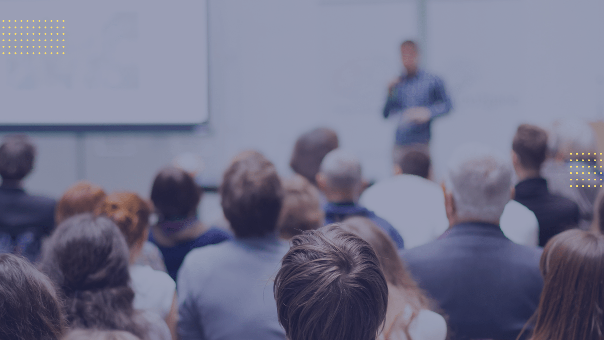 Group of people sitting in a presentation setting, looking at a speaker in front of the room.