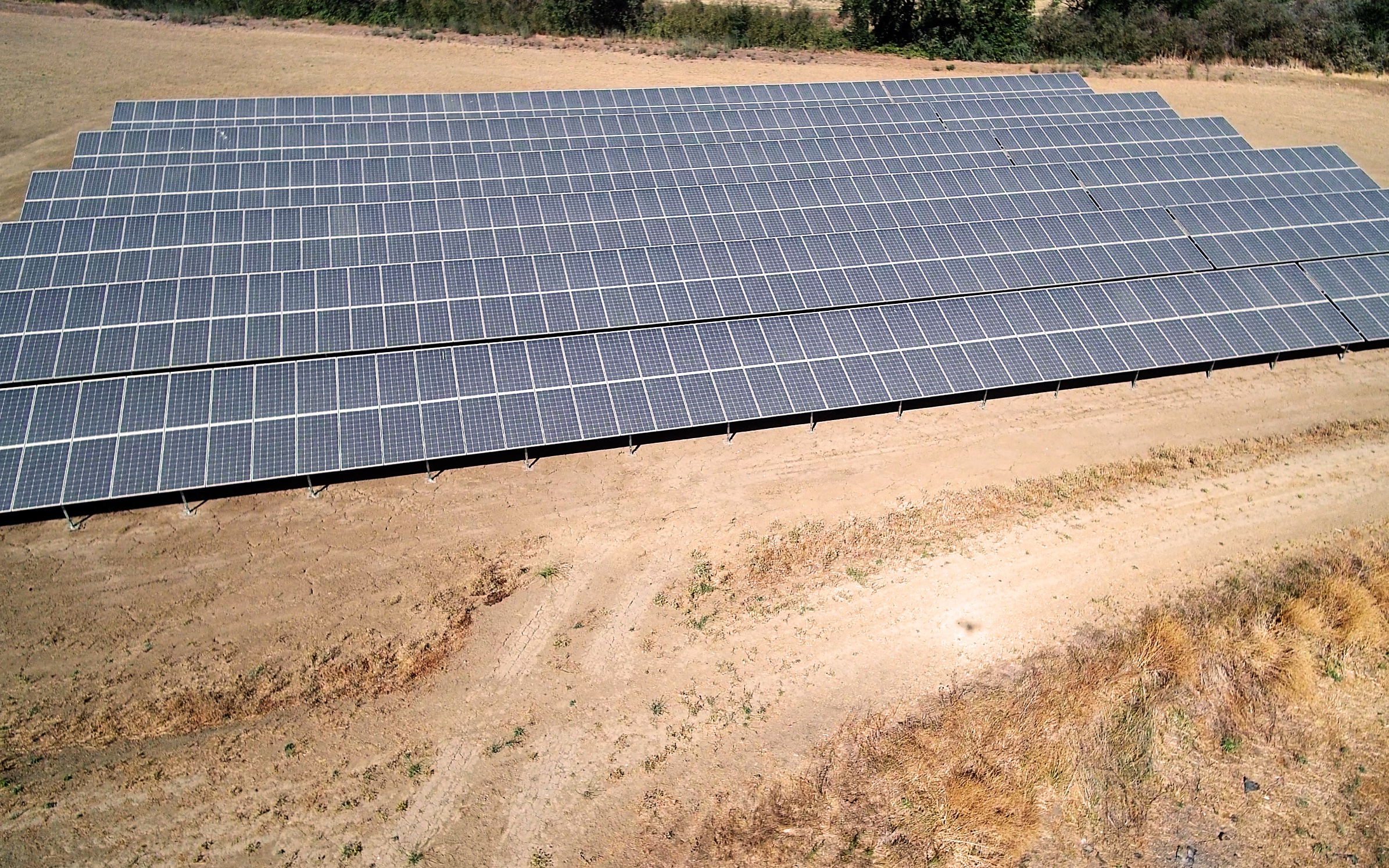 A close-up view of a large ground-mounted solar panel system installed in an open rural area. The reflective blue solar panels are aligned in rows, capturing sunlight for energy production.