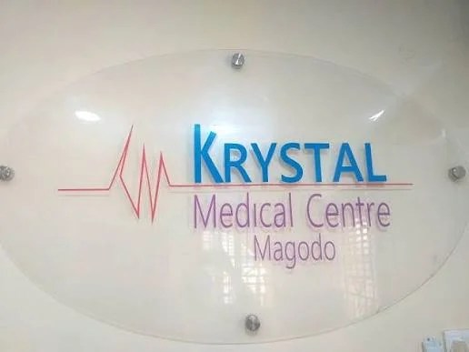 Sign for KRYSTAL Medical Centre Magodo on a glass plaque with blue KRYSTAL text and a red ECG waveform logo