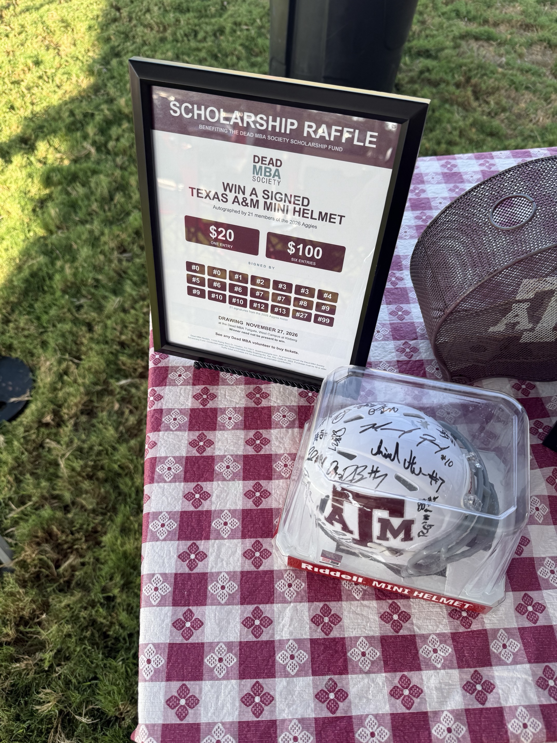 The signed Texas A&M mini helmet on the Dead MBA tailgate table next to the Scholarship Raffle sign
