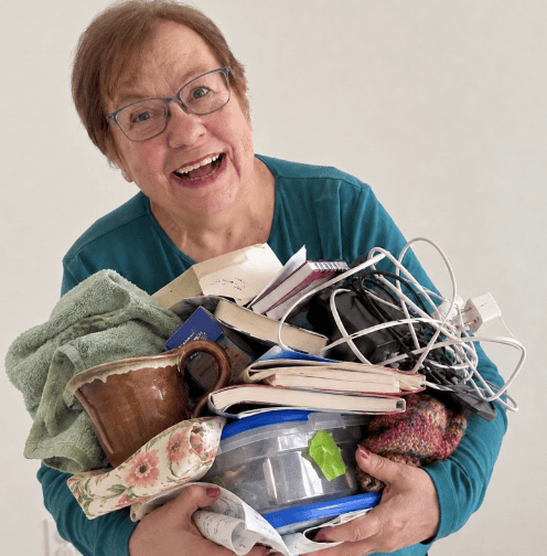 Older, light-skinned person with glasses, holding a variety of items (clutter)