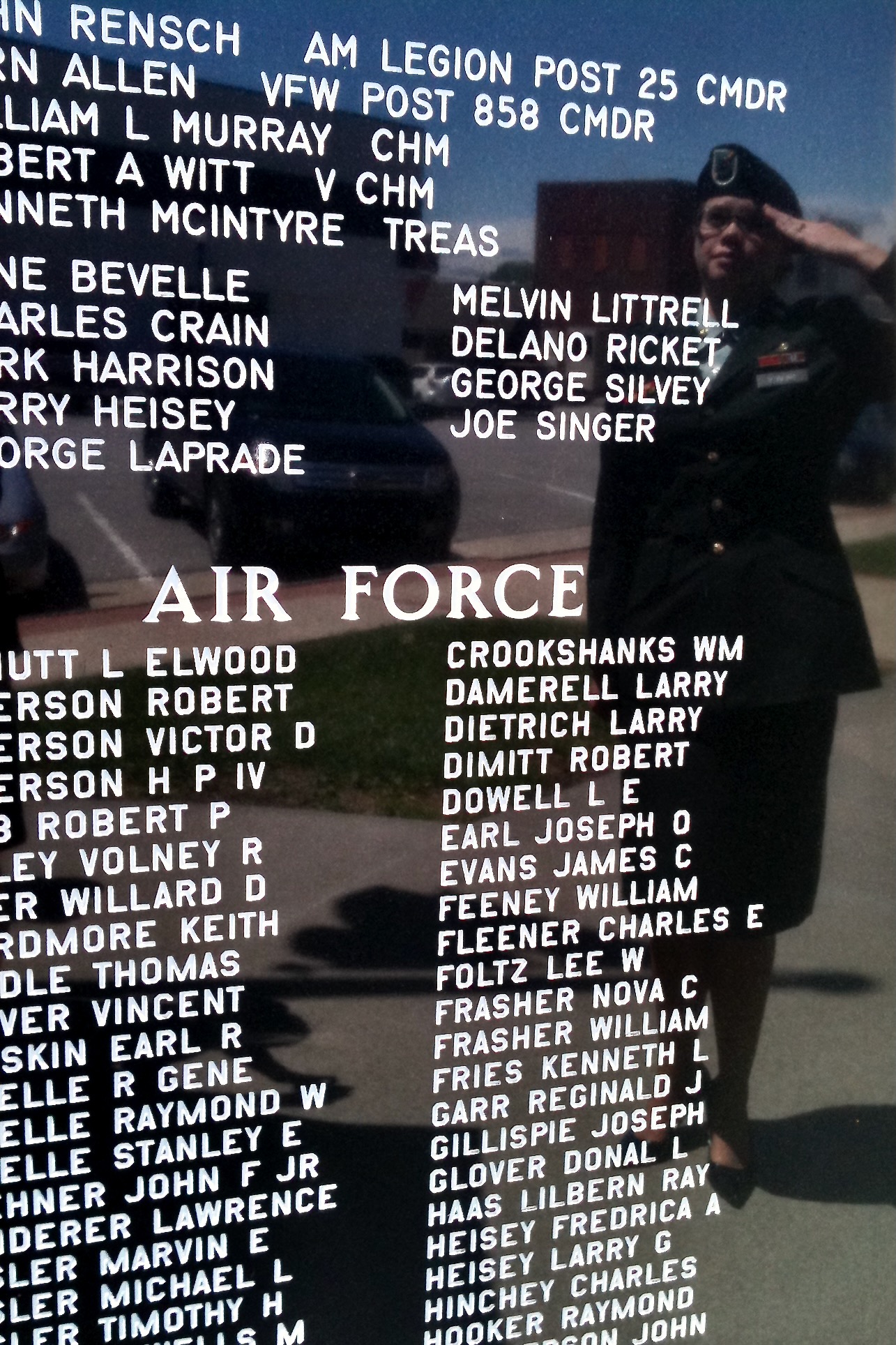 Reflection of a female soldier in US Army dress uniform saluting a black marble military monument, showing her grandfather's name for an inspirational Father's Day and Memorial Day reflection.