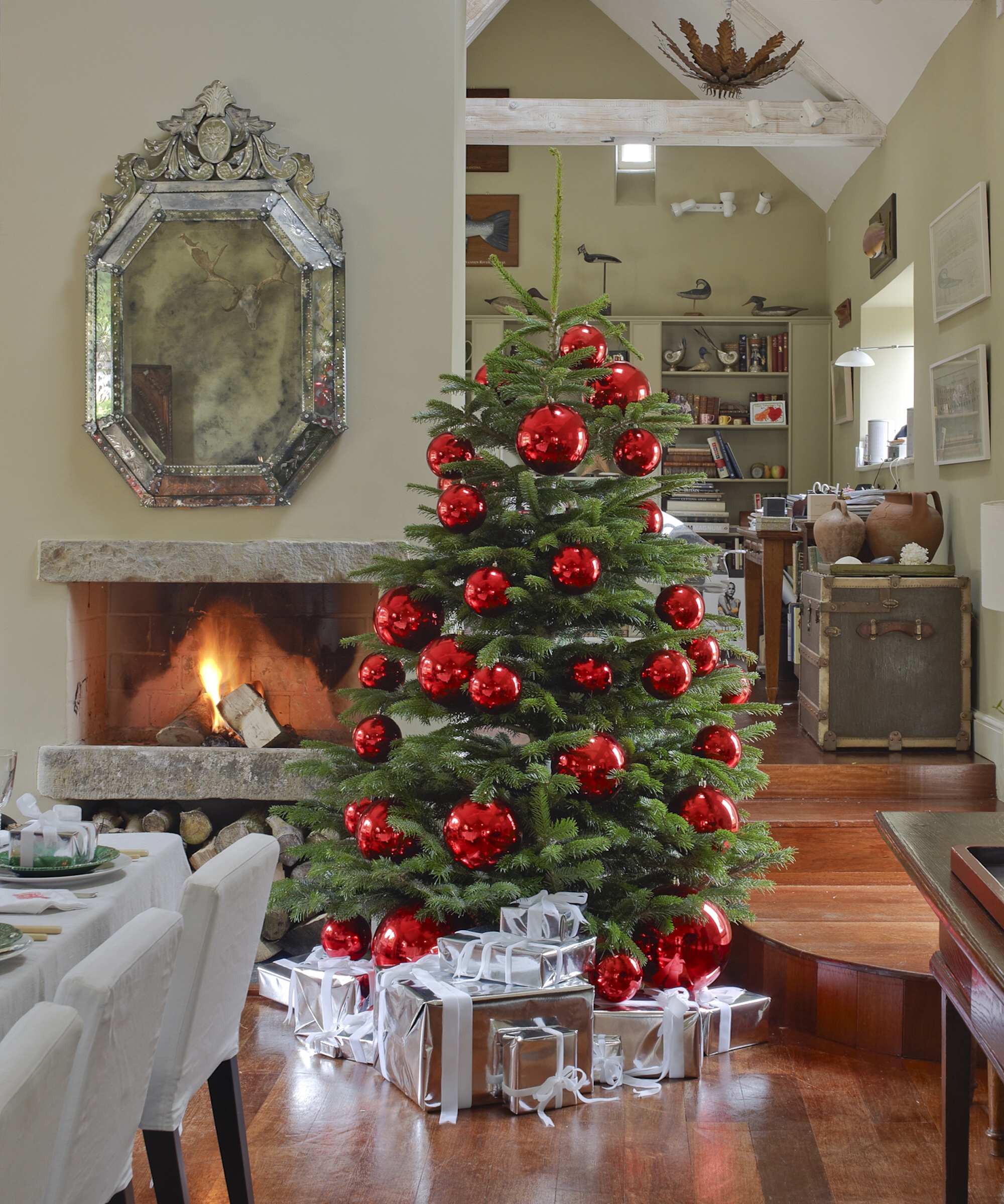 Open plan dining room with lit open fireplace, Christmas tree decorated with red baubles, presents, venetian mirror, vaulted ceiling with beams H&G 12/2012