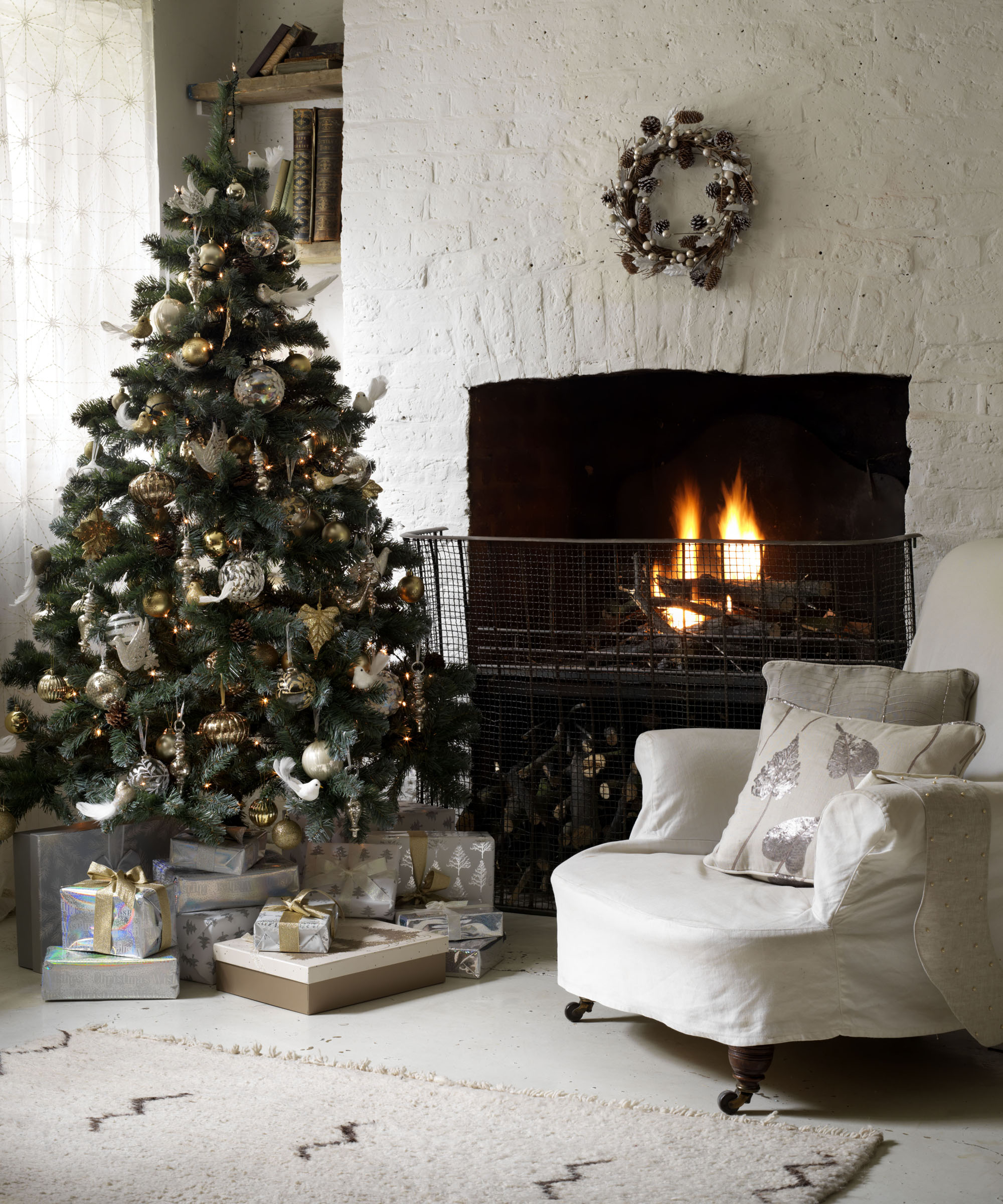 All white living room, Christmas tree, painted brick wall chimney breast, lit fireplace, armchair, wreath above fireplace, rug CH&I 12/2011 pub orig