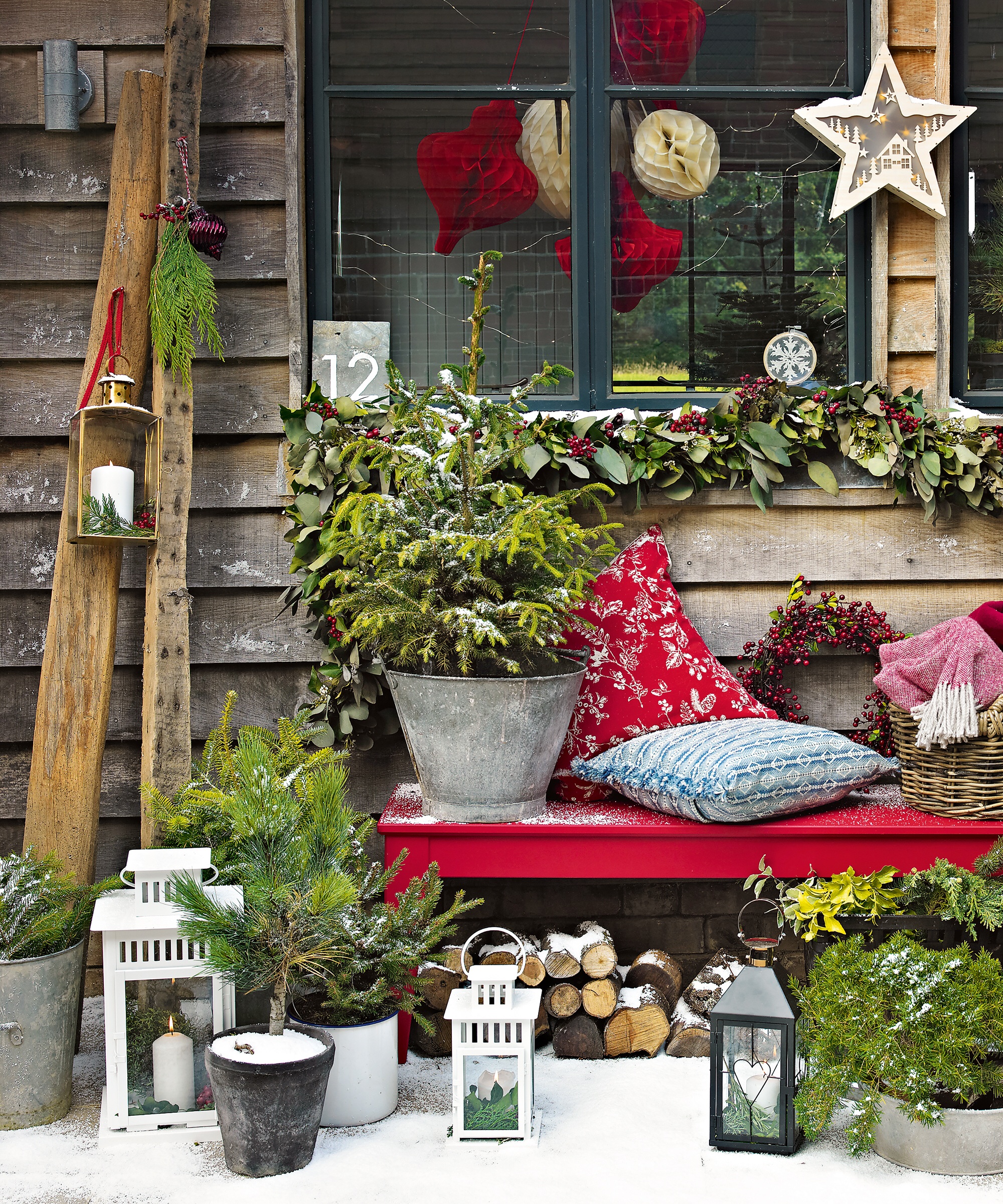 Christmas decorations, an outdoor bench with light snow cover, cushions, Christmas tree baubles and stars. Candle lanterns.