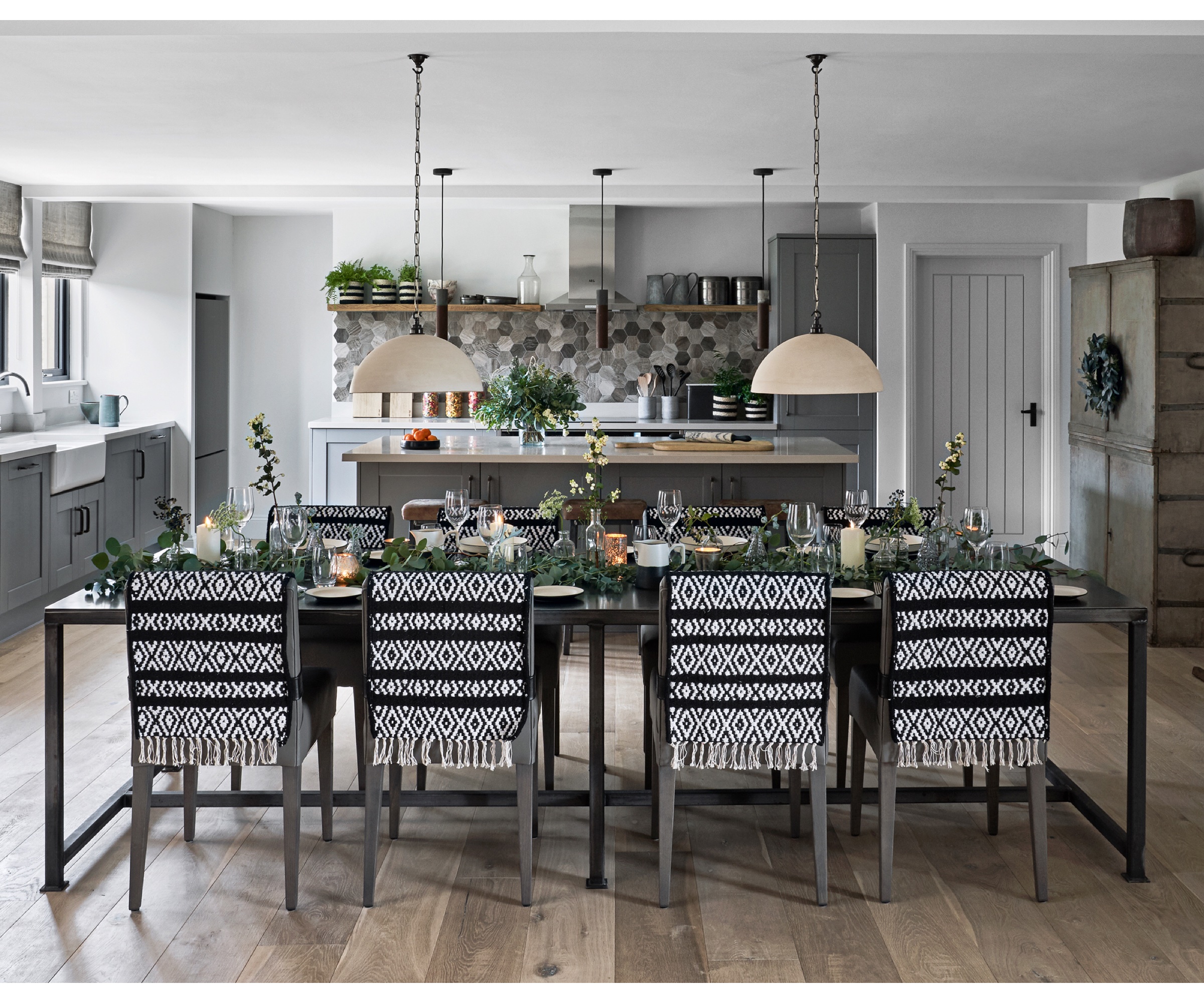 Large kitchen diner with kitchen island, wooden flooring and long dining table laid for a meal with fabric throws on each chair. Converted farm buildings, a family home on a farm in the Cotswolds, home of George and Polly Phillips and their baby