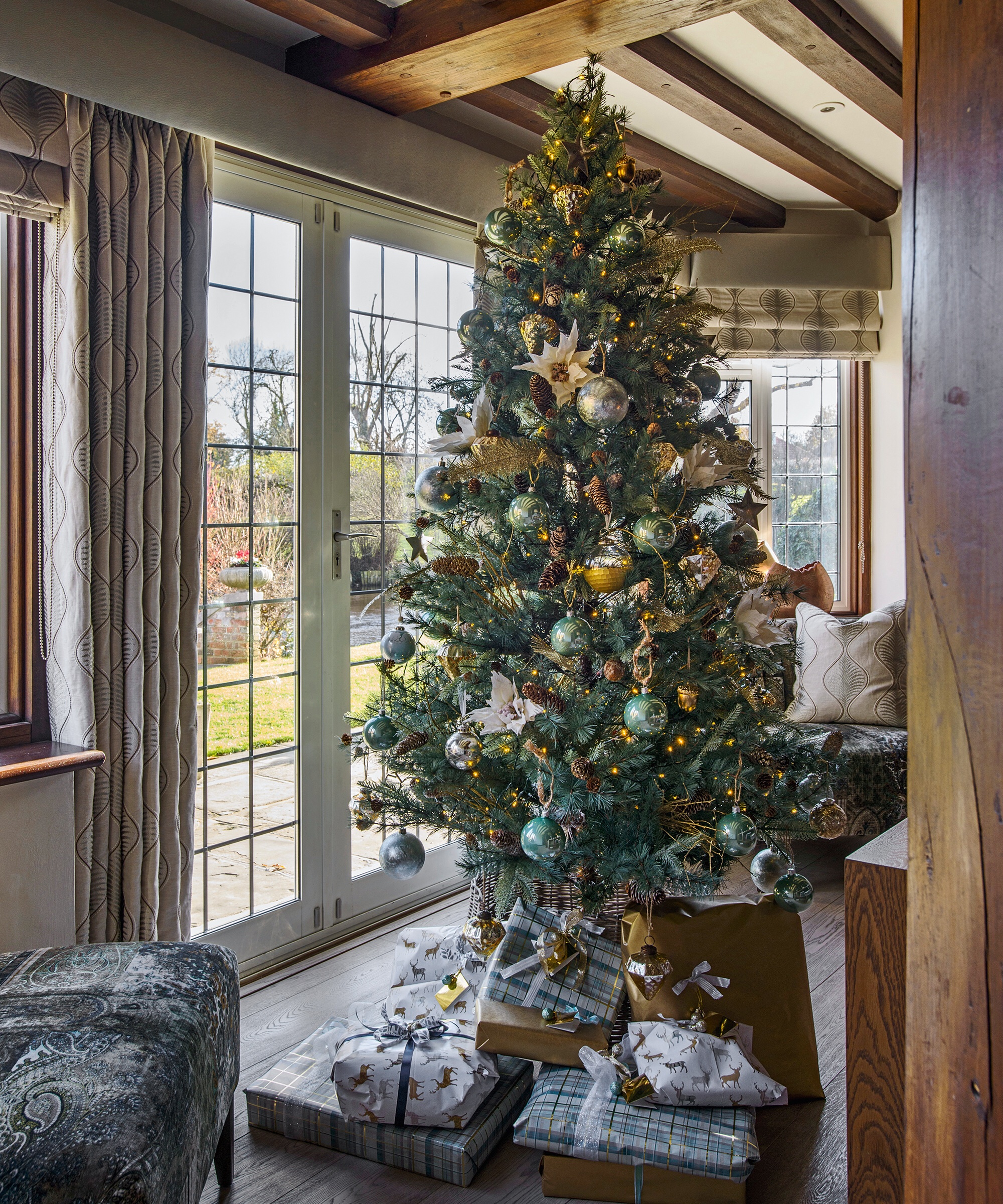 Decorated Christmas tree beside leaded french doors and below a beamed ceiling. A 16th century house with five bedrooms and a moat, home of Lynsey and Paul Cross and their family in Essex.