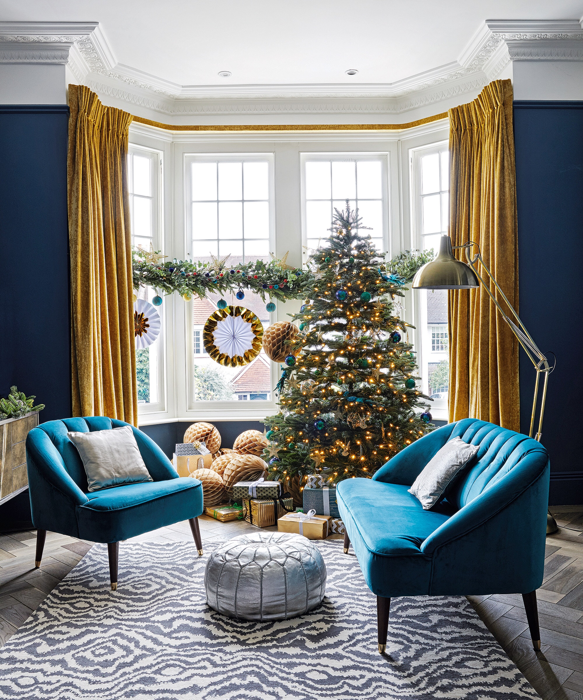Living room with two chairs with bright blue velour covers, patterned rug, dark navy blue walls and rich dark yellow curtains and a Christmas tree. A renovated Victorian house in London, home for Sue and Matt..