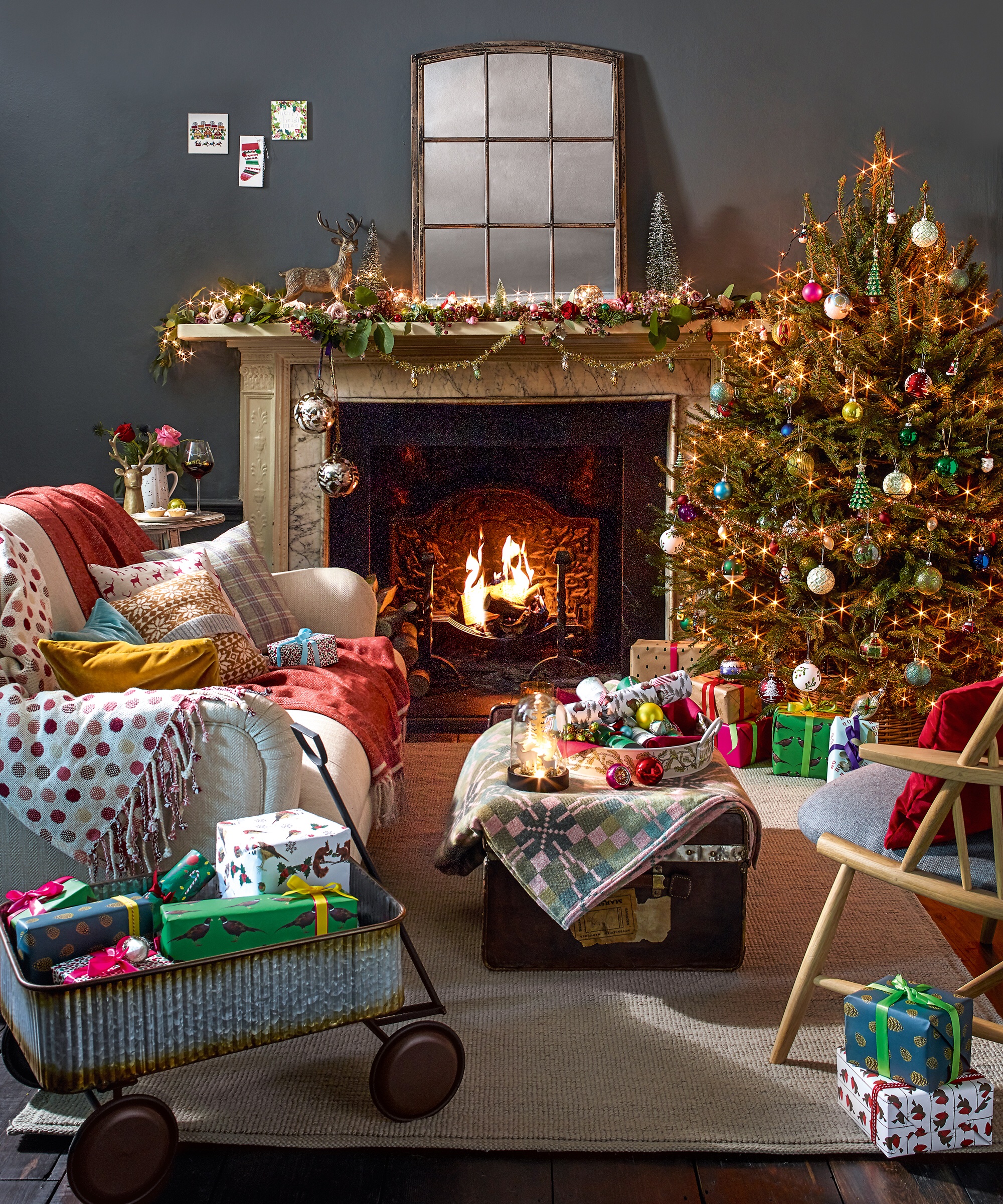 Living room with a mantlepiece and fireplace with a lit fire, a Christmas tree and sofa and table, and toys and presents. Pub Orig