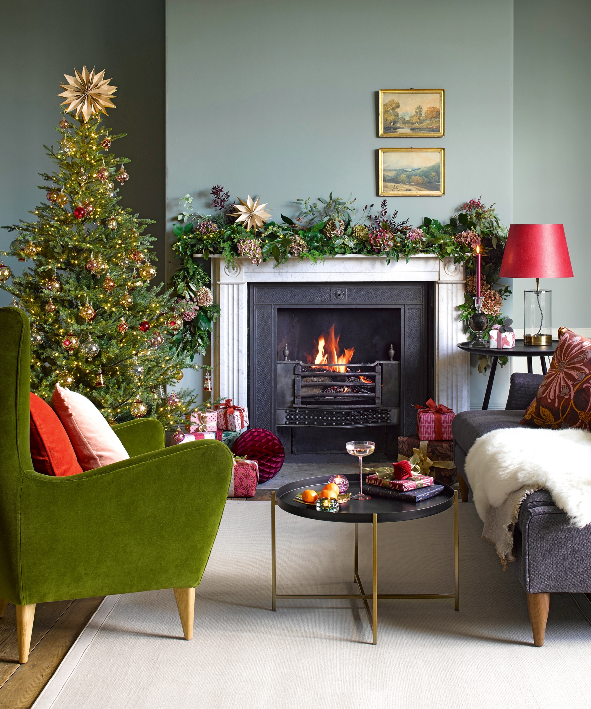 Decorating ideas. Christmas comes home. Living room with mid-century modern sofa and armchair in front of fireplace decorated with garland, Christmas tree in corner.