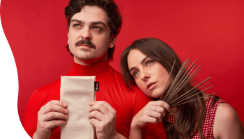 Photo of a man and woman in red turtlenecks against a red background, both with deadpan expressions, the man holding a canvas Moody pouch and the woman holding a fanned bundle of incense sticks
