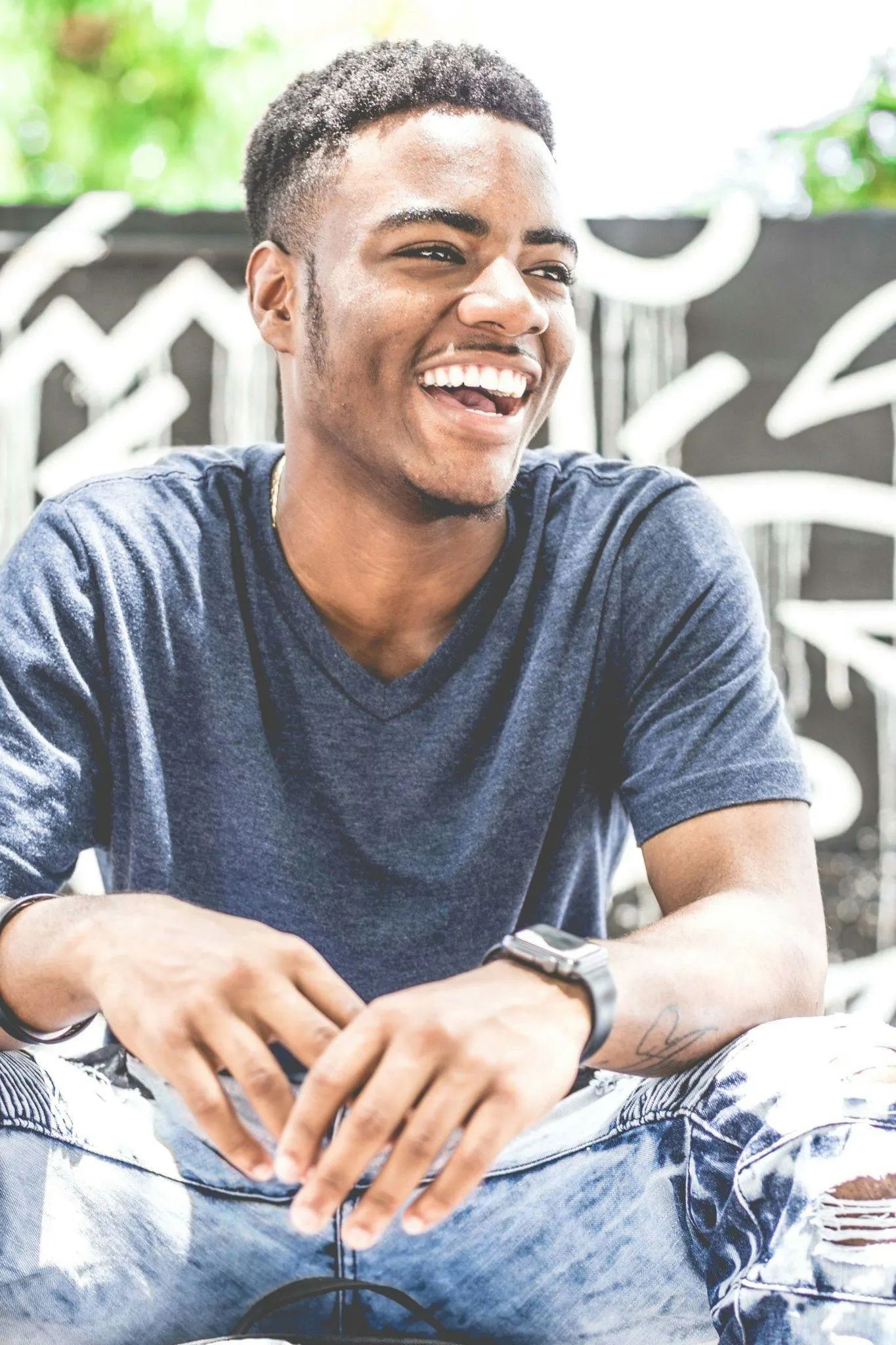 Portrait of a smiling young man wearing a blue t-shirt, sitting casually outdoors.