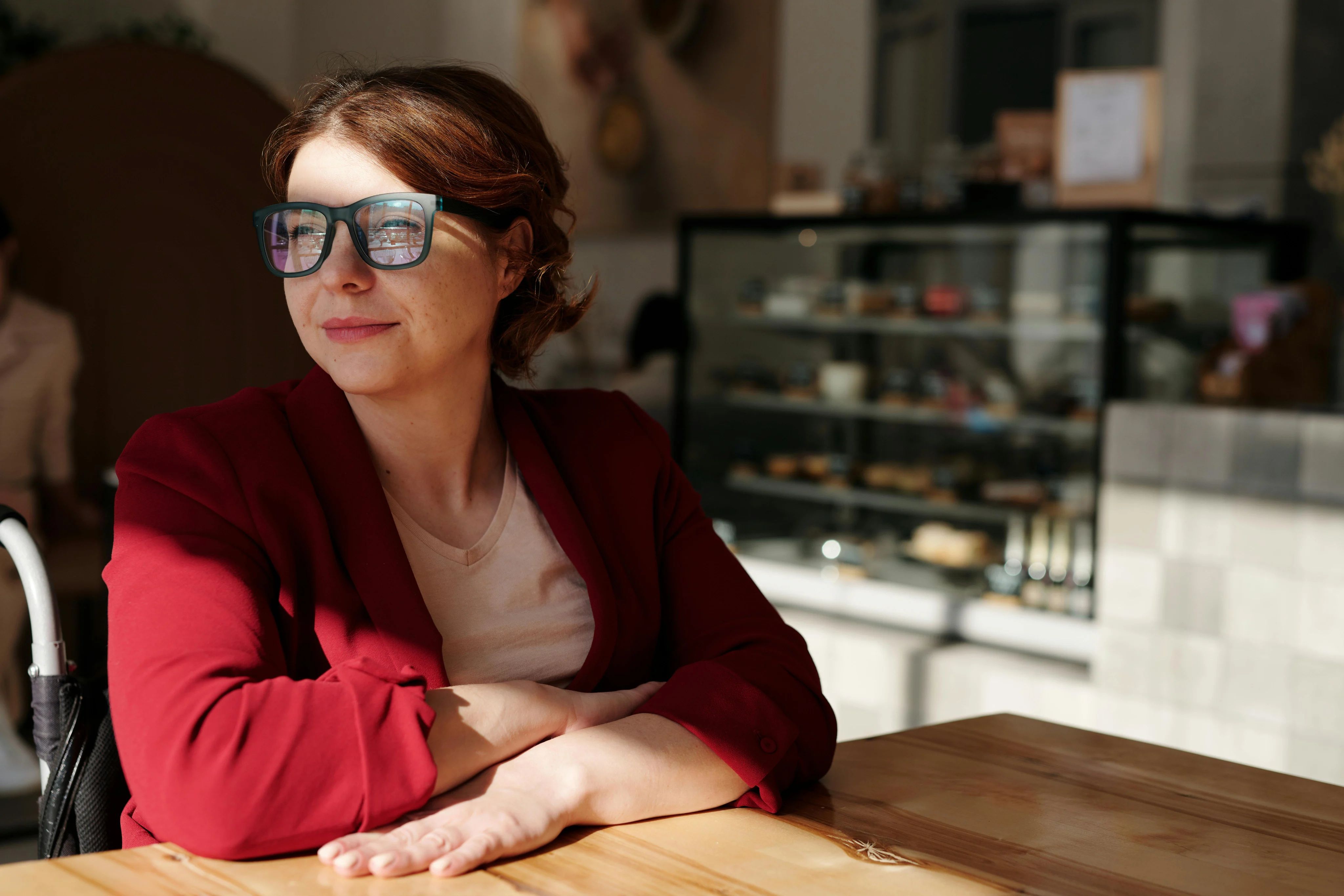 Professional woman in a red blazer and glasses sitting at a wooden table in a modern coffee shop