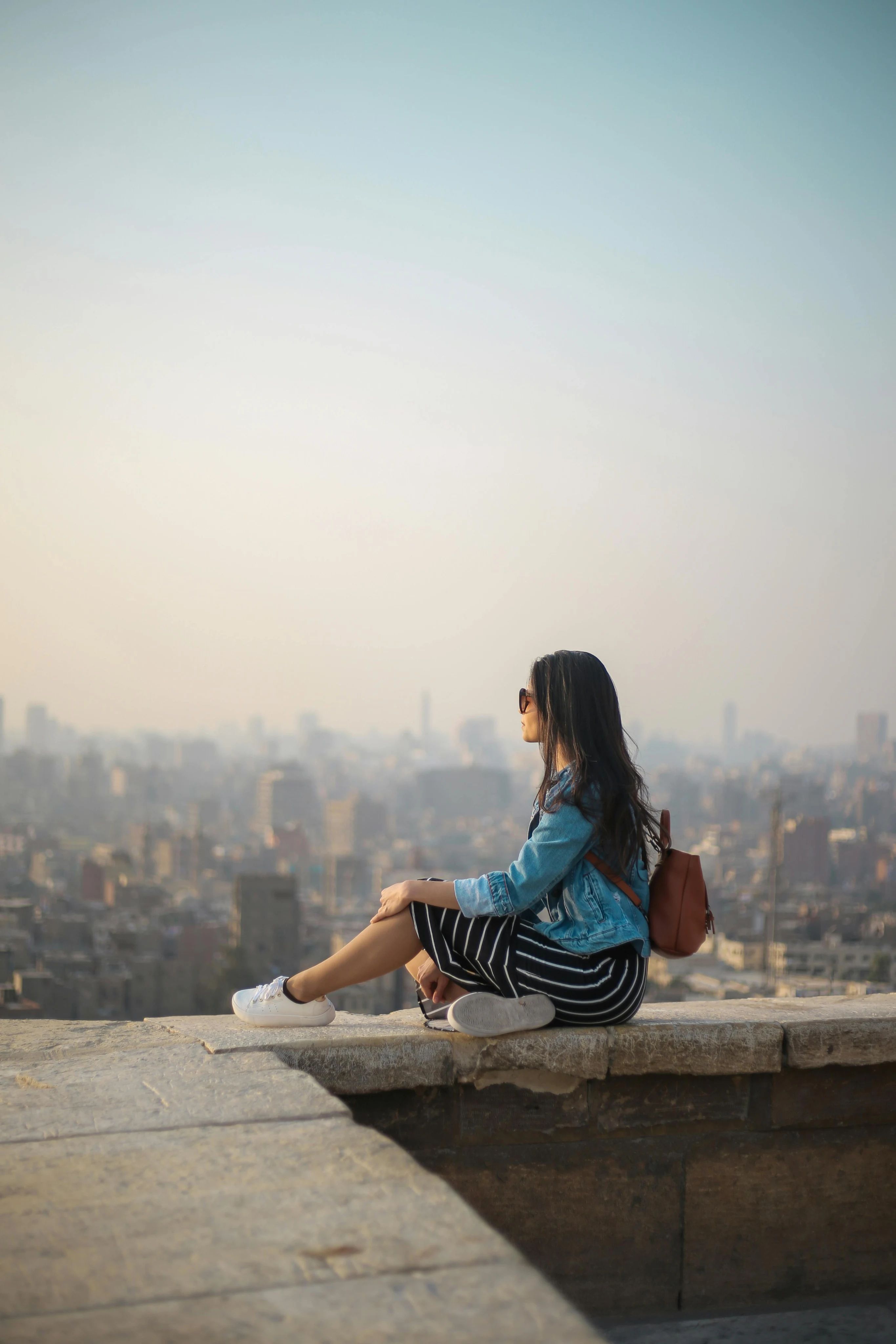 A woman sitting on a ledge overlooking a city skyline.