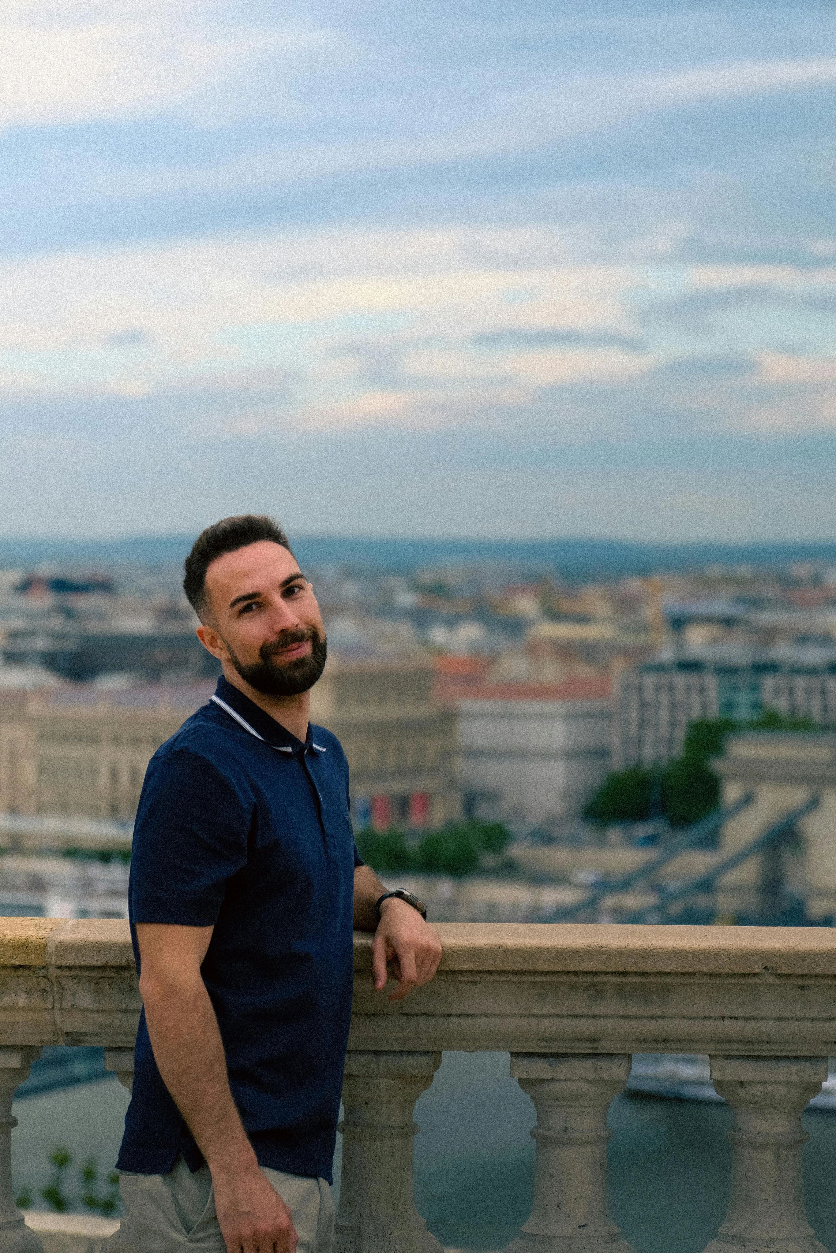 A smiling man posing with a city landscape in the background.