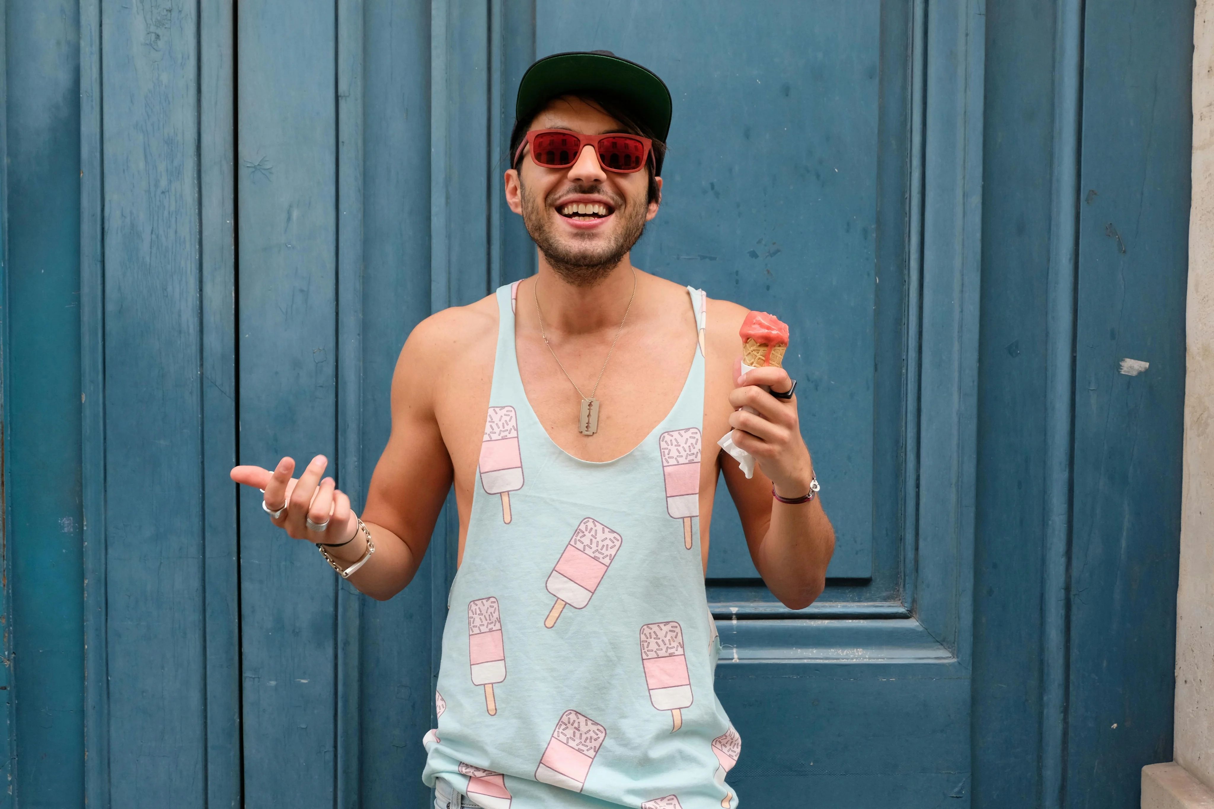 Cheerful man in a casual tank top enjoying ice cream in front of a vibrant blue door