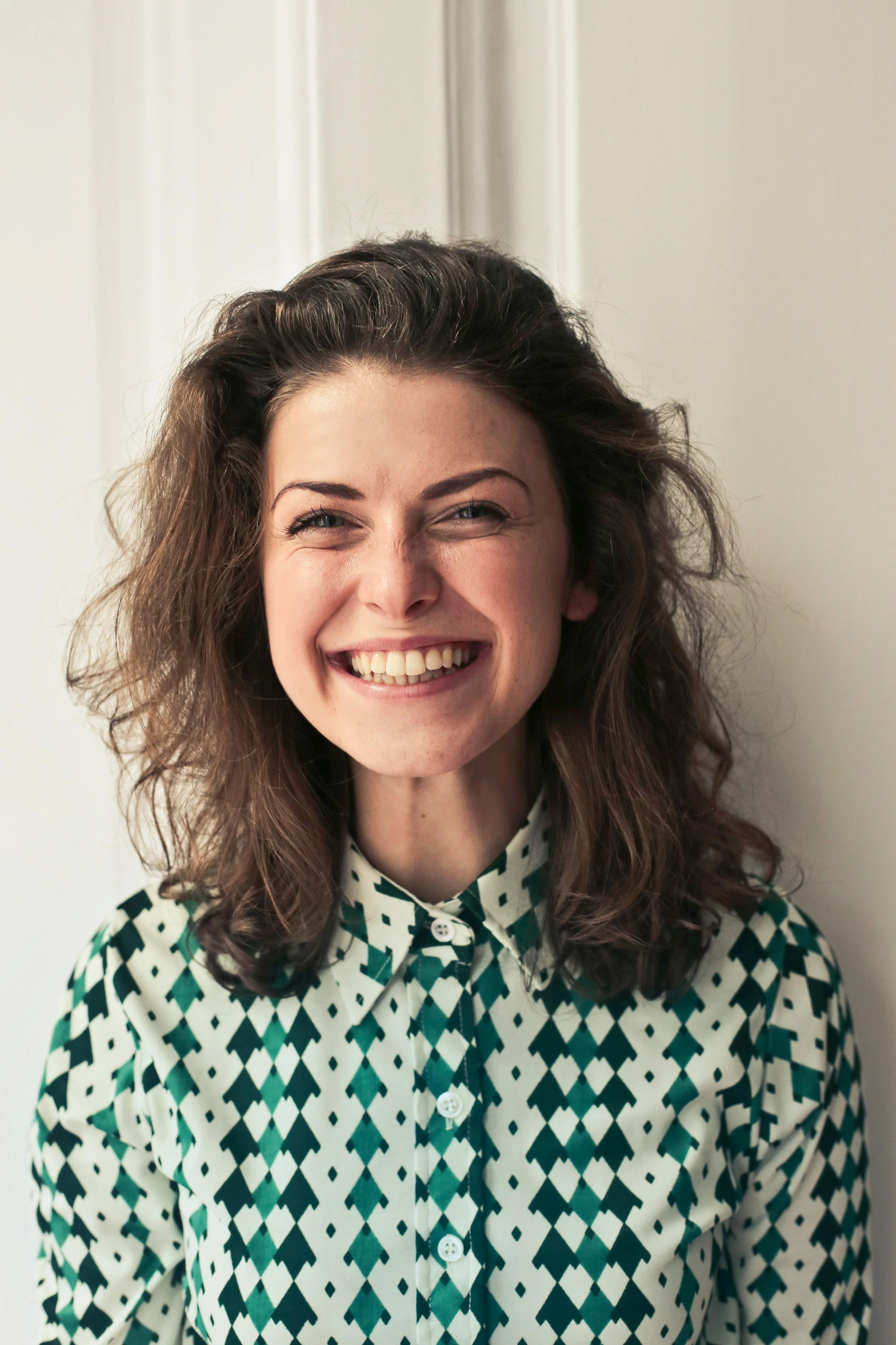 A smiling woman with curly hair wearing a green patterned shirt.