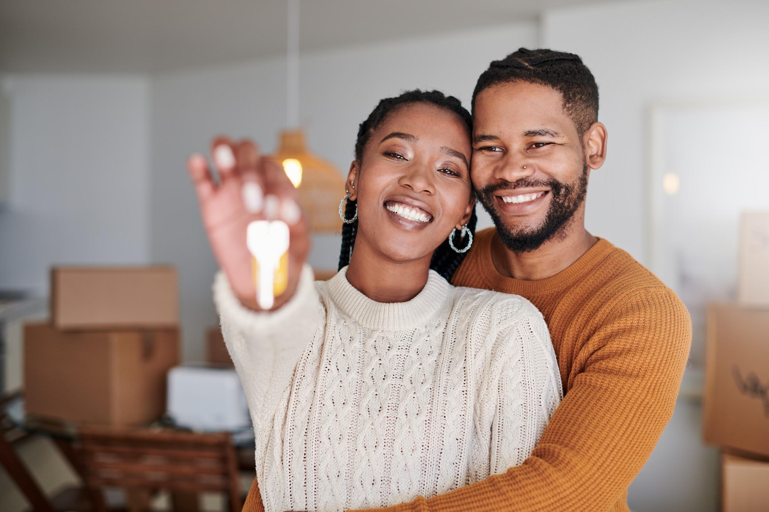 A young Black man embraces a young Black woman as she holds a key in the air.