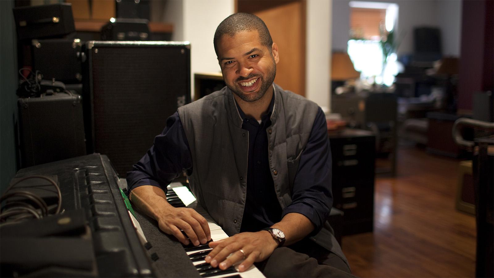 Jazz great and HSPVA alum Jason Moran smiles while posing seated at a piano.