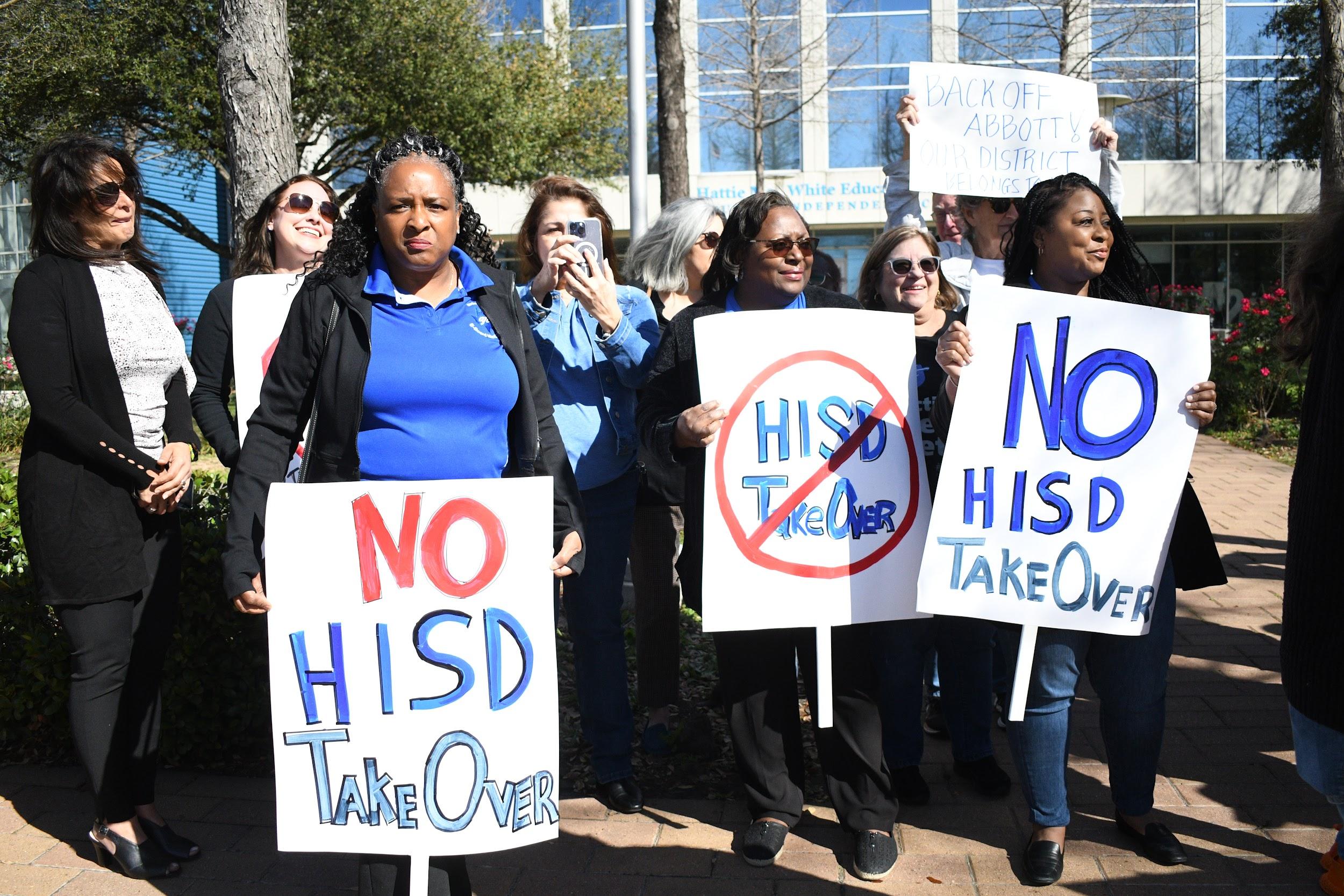 Three women hold protest signs while attending a rally to protest the TEA takeover of Houston ISD.