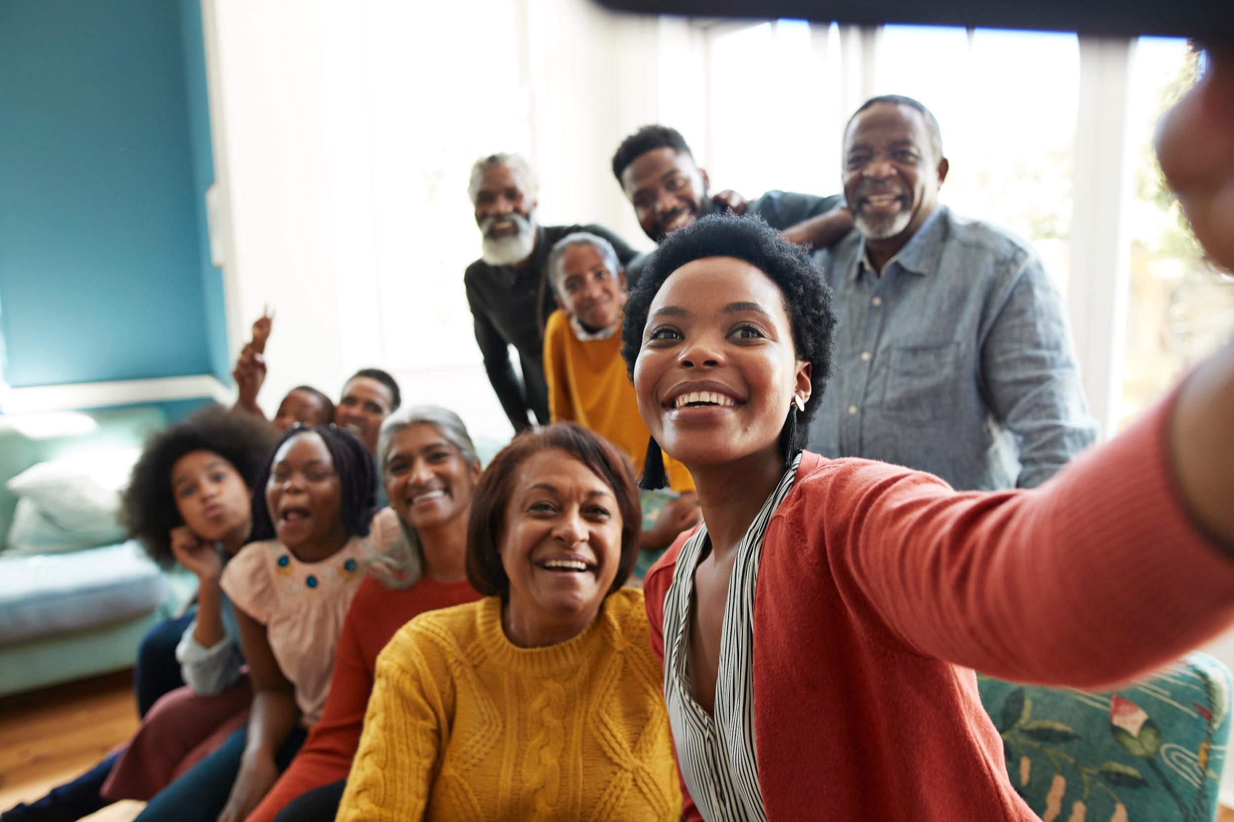 Smiling young woman taking selfie with family and friends. Smiling young woman taking selfie with family and friends. Getty Images.