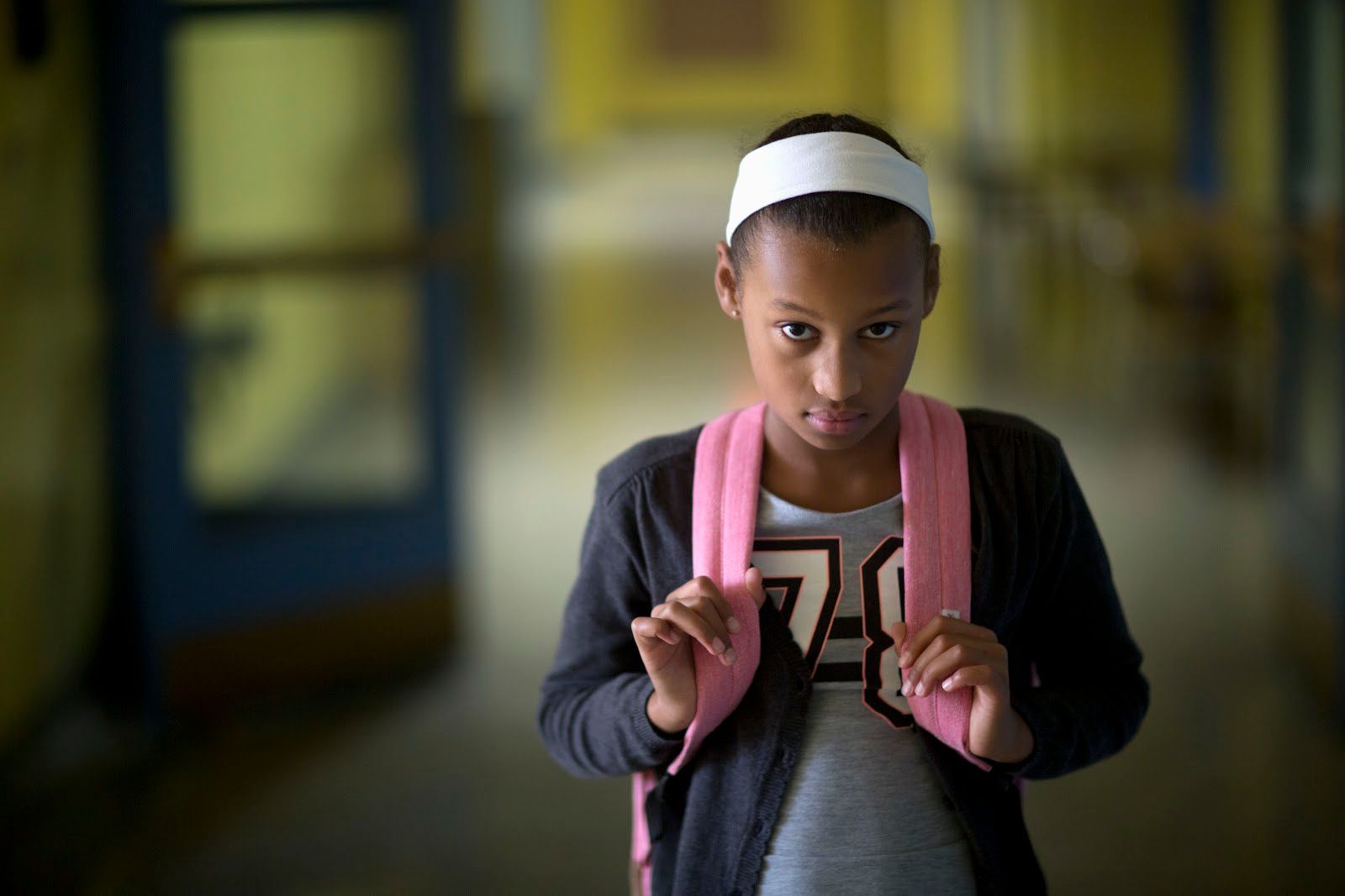 Middle school-aged Black girl in school hallway looking sullen.