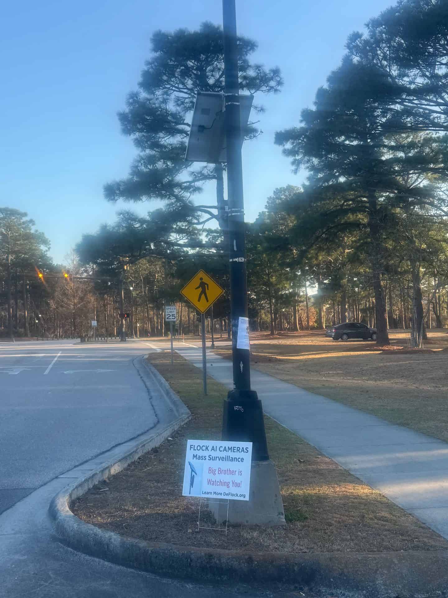 Flock camera on a black pole near UNCW in Wilmington, solar panel on top, at a 25 mph crossing