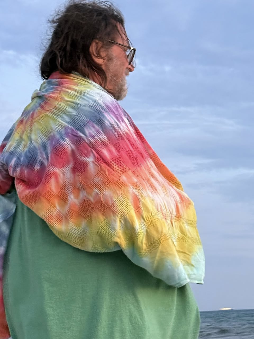 Photo of a human male wearing glasses and a multi-colored knitted blanket over their shoulders.