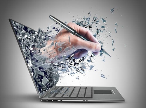 Hand holding a pen emerging from a shattered laptop screen, with glass fragments flying outward.