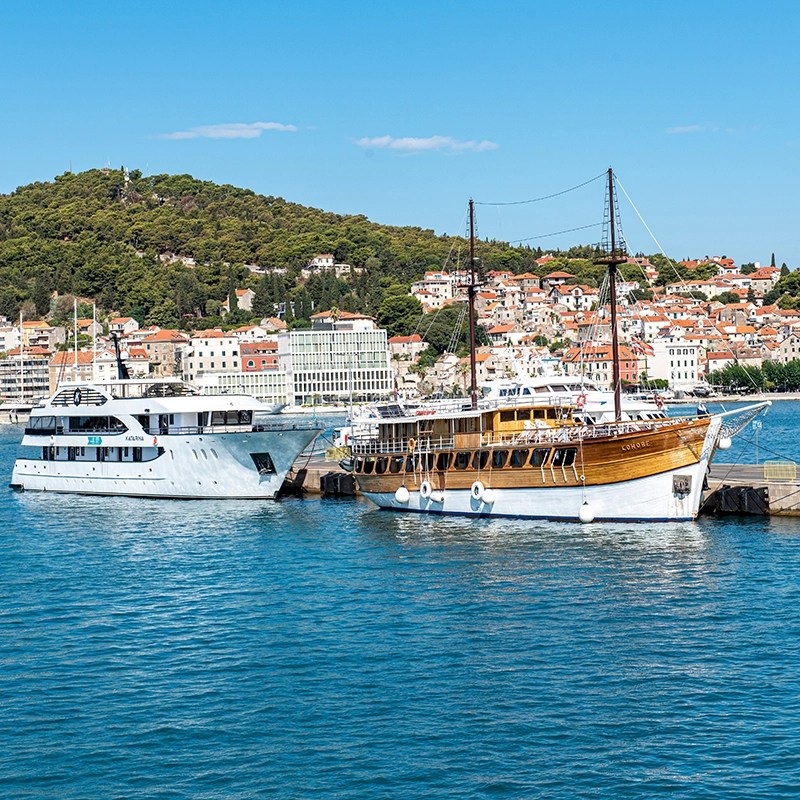 Barcos atracados no porto de Split, Croácia, com casas na encosta ao fundo sob um céu azul claro.