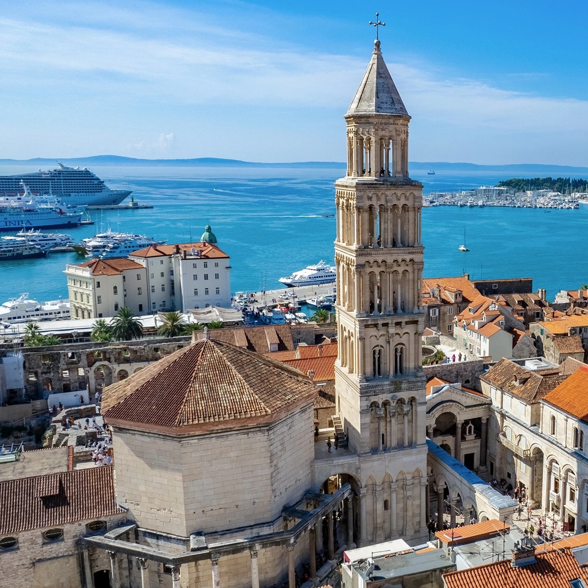 Uma vista panorâmica de Split, Croácia, com a Catedral de São Dômnio, sua torre sineira e edifícios históricos ao lado das águas vibrantes e azuis do Mar Adriático.