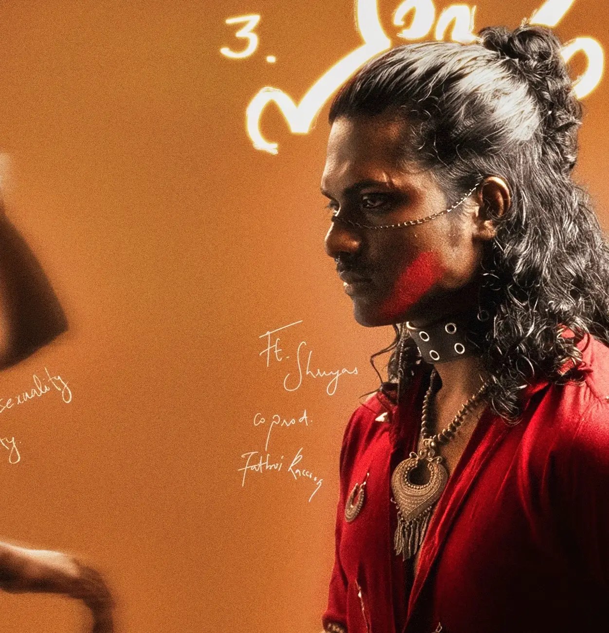 Aksomaniac in red attire with jewelry and face chain, from the song “Paapam” featuring Shreyas on the Varthamanam EP cover art.