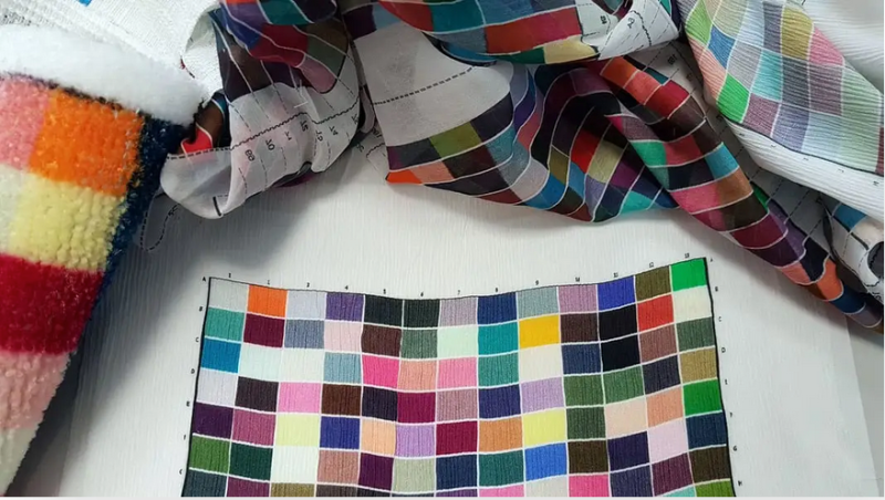 Colorful fabric swatches arranged in a grid plus folded patterned cloth on a white surface, with a measuring tape nearby.