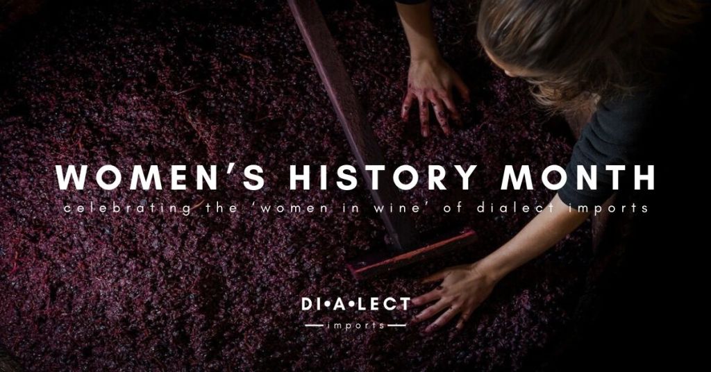 A close-up image of a woman's hands working with grapes during the winemaking process, with the text 'WOMEN'S HISTORY MONTH celebrating the women in wine of dialect imports' overlaying the image.