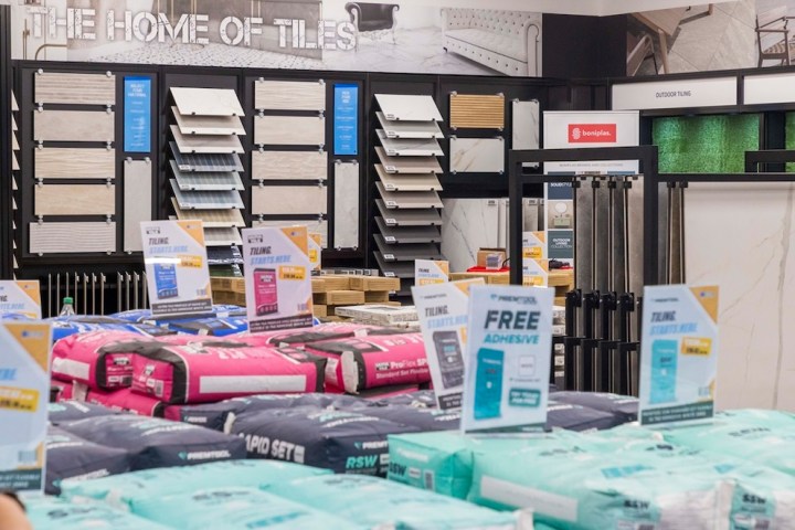 A display of various tile samples at a home improvement store, featuring colorful bags of adhesive and promotional signs for tiling products.