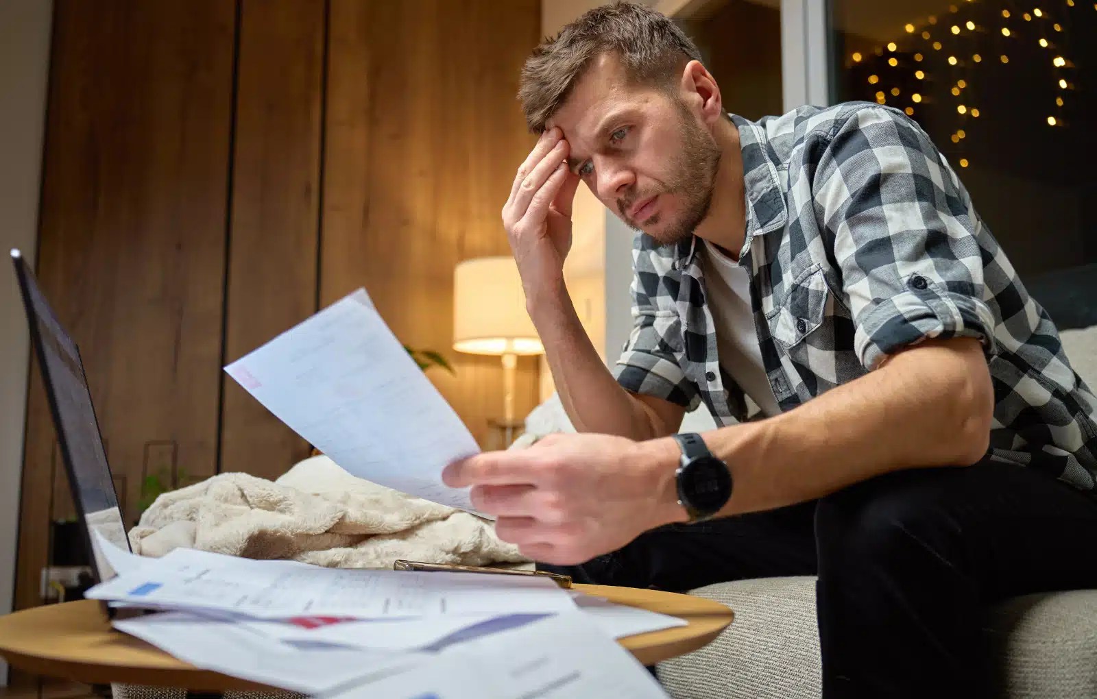 Owner operator sitting on his couch at home looking stressed at bookkeeping paperwork and receipts
