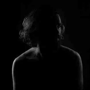 Silhouette of a person with shoulder-length hair against a black background. The lighting outlines the face and shoulders, crafting a dramatic, mysterious effect that mirrors the chaos of time-blindness, capturing an elusive struggle against overwhelming moments.
