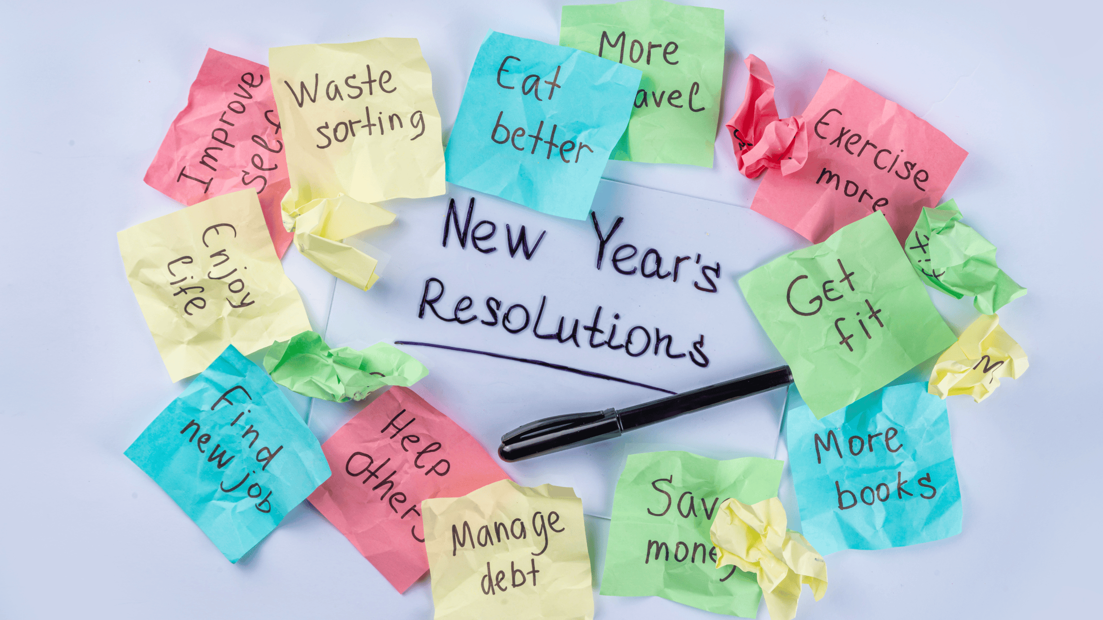 A circle of colorful sticky notes with New Years resolutions, emphasizing realistic goals for mental well-being, surrounds a pen. Notes include: Improve self, Eat better, Waste sorting, more travel, Exercise more, Enjoy life, Find a new job, Help others, Manage debt, Save money, Get fit, and More books.