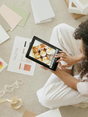 Woman using tablet surrounded by design tools and gift box, showcasing creativity and online work.
