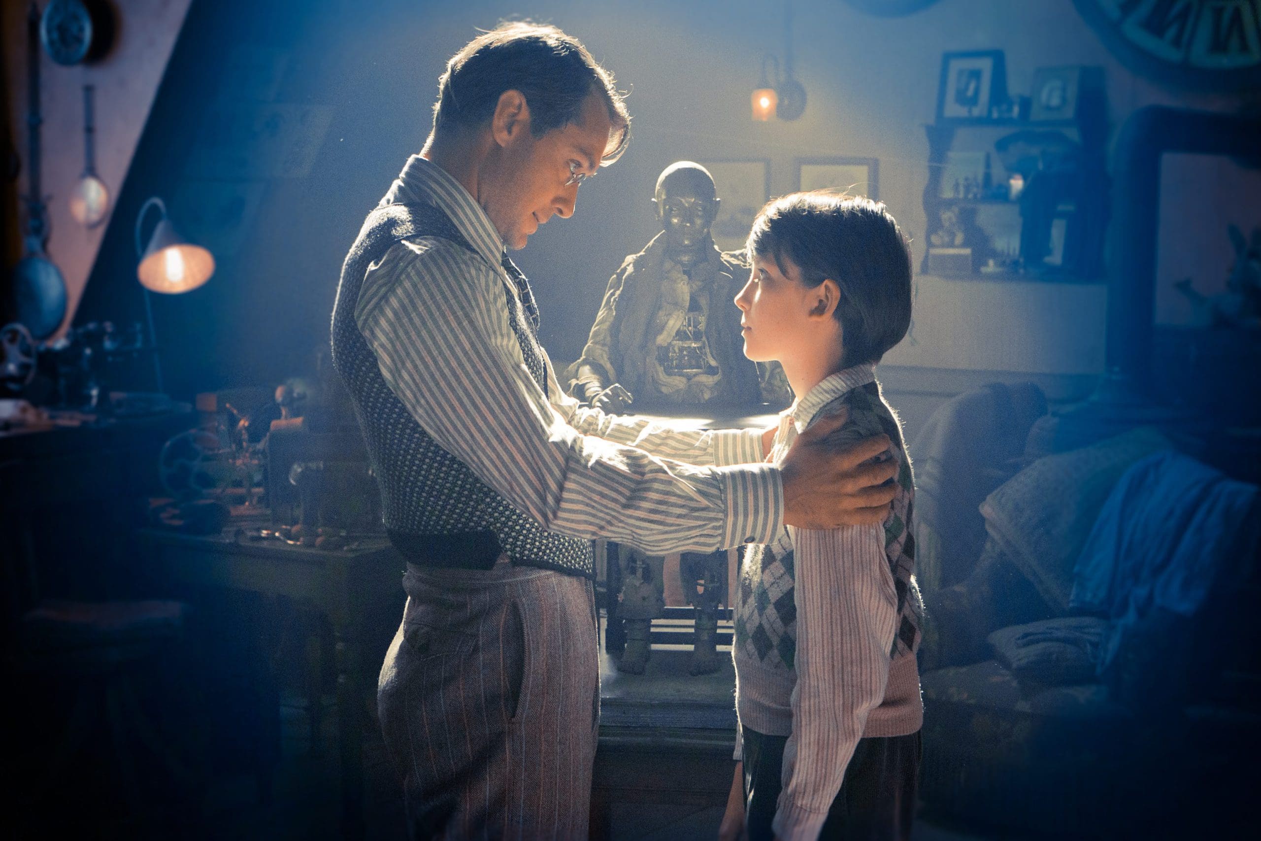 An adult man and a boy interacting warmly in a dimly lit room.
