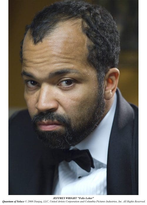 A close-up portrait of a man with a beard and short hair, wearing a tuxedo with a bow tie. He has a serious expression, looking off-camera against a softly blurred background.