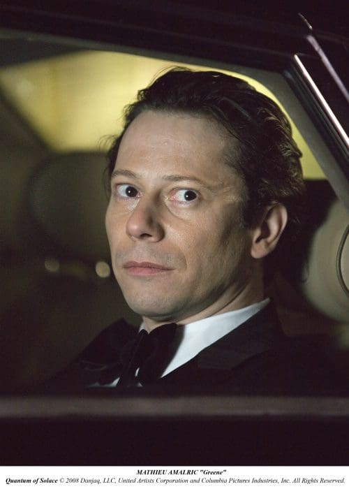A man with light brown hair and a tuxedo sitting in a car, looking thoughtfully out the window. The interior is dimly lit, enhancing the serious expression on his face.