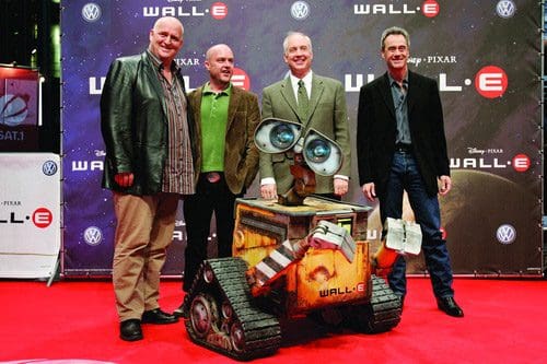 Four men posing together at a premiere event, standing on a red carpet with a prominent backdrop featuring the title "WALL-E." A robotic character, WALL-E, is featured in front of them, showcasing its expressive eyes and unique design.