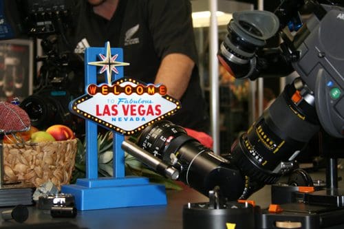 A colorful model of the iconic "Welcome to Fabulous Las Vegas" sign stands on a table surrounded by cameras and photography equipment, with a person partially visible in the background.