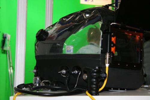 A close-up of a black and clear medical device designed for patient treatment. It features various knobs and hoses, with a glossy transparent panel showing inner components, set against a green background.