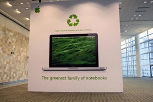 A large promotional display featuring a laptop with a green grass background. Above the laptop, a recycling logo is visible. The text at the bottom reads, 'The greenest family of notebooks' with a note about recyclable materials.